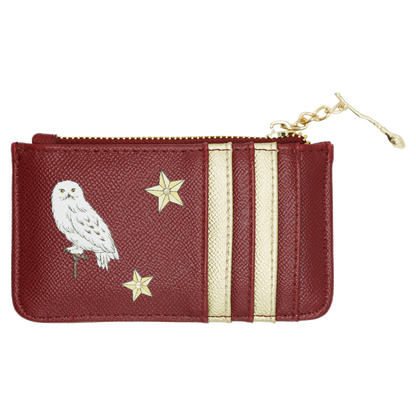 A small zip-around pouch in textured burgundy leather with cream vertical stripes, a white Hedwig applique, and two gold stars. A Nimbus 2000 charm is attached to the zipper.