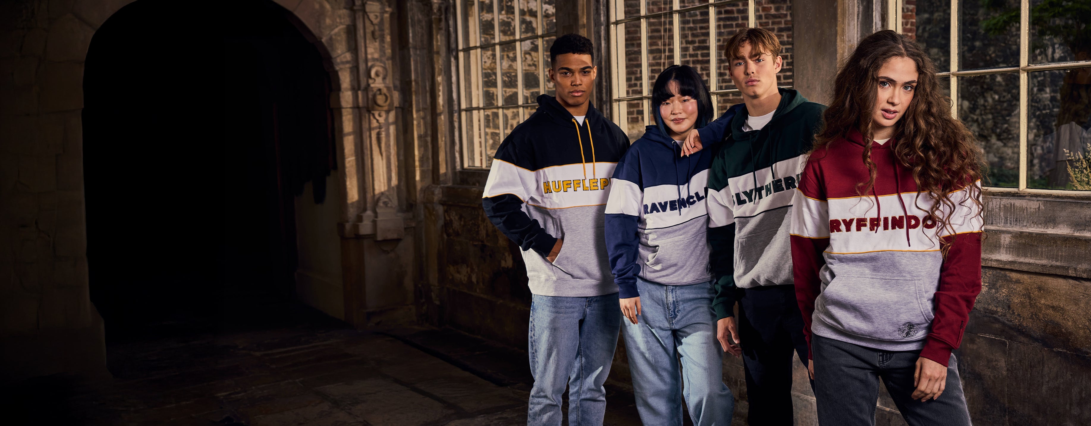 Four individuals wearing Harry Potter-themed sweatshirts standing in front of a stone wall.