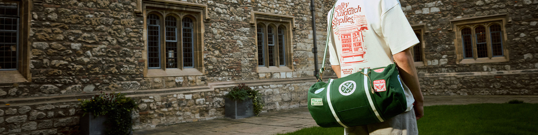 Person carrying a Quidditch duffle bag with patches in front of a stone building