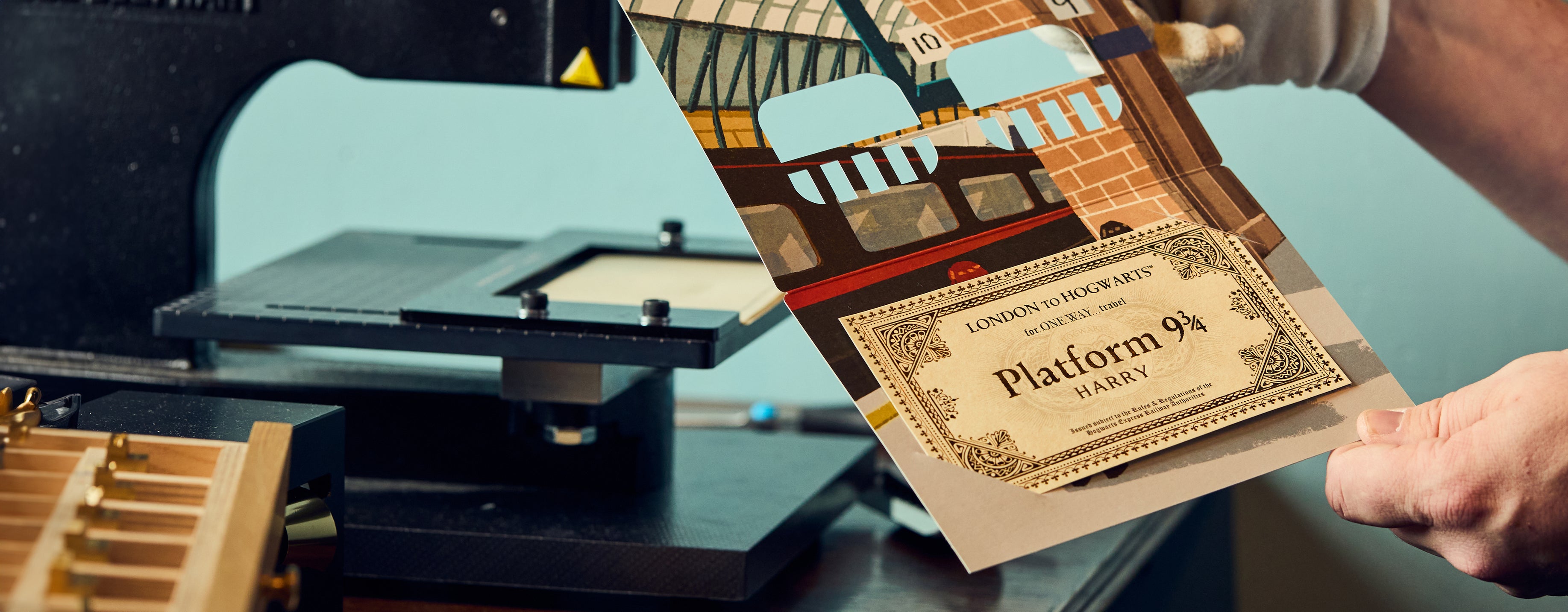 Person holding a printed Hogwarts Express ticket with a train station design, next to a printer.