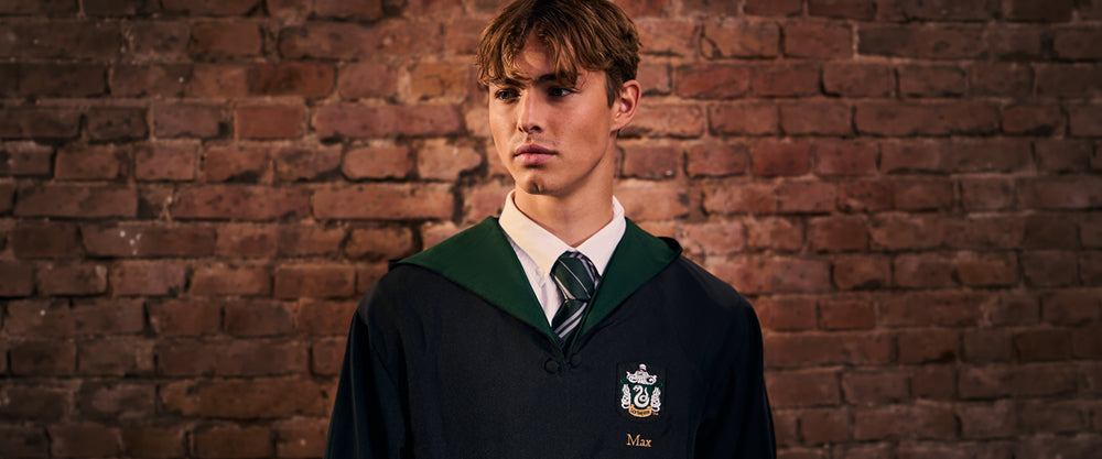 Person wearing a Slytherin robe with a school emblem against a brick wall.
